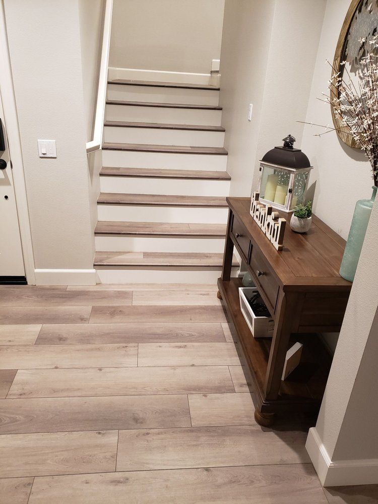 A hallway with light wood flooring, a wooden console table with a decorative lantern, and carpeted stairs leading upward.