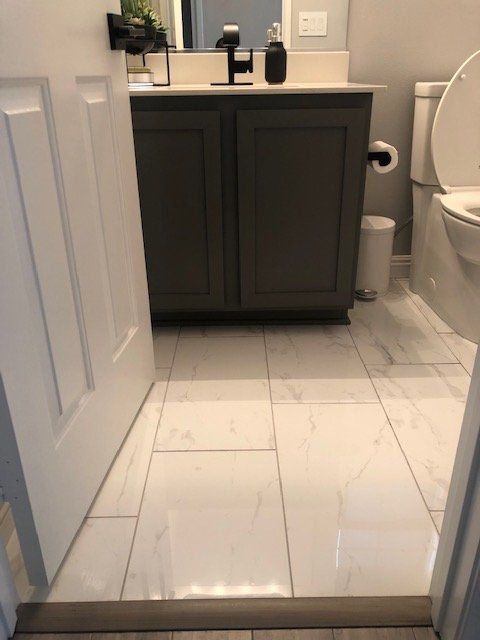 A view into a bathroom with a dark gray vanity, white marble-look floor tiles, and a white toilet.