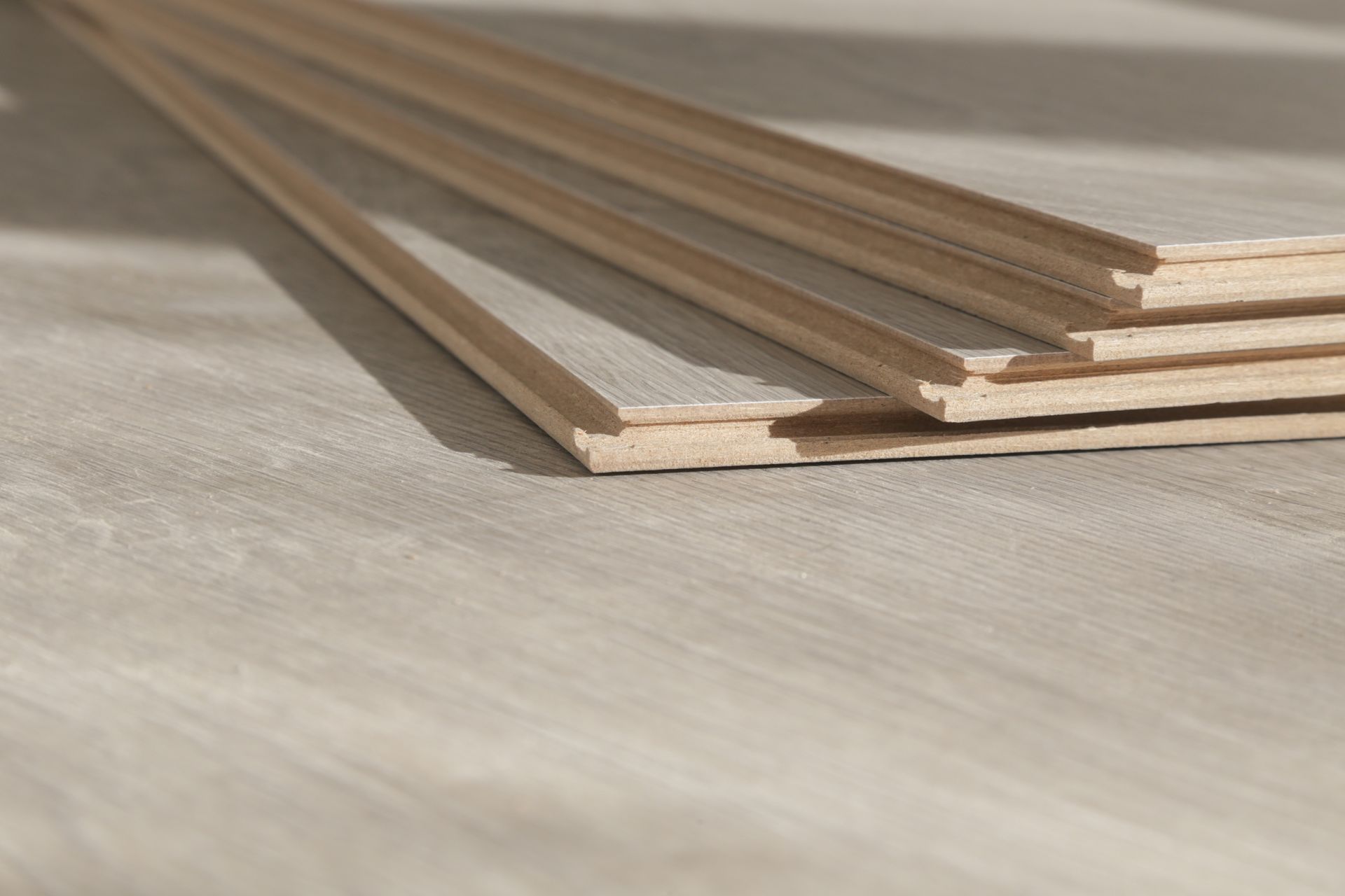 Wooden flooring planks, stacked with exposed edges, sit on a wood-grain surface.