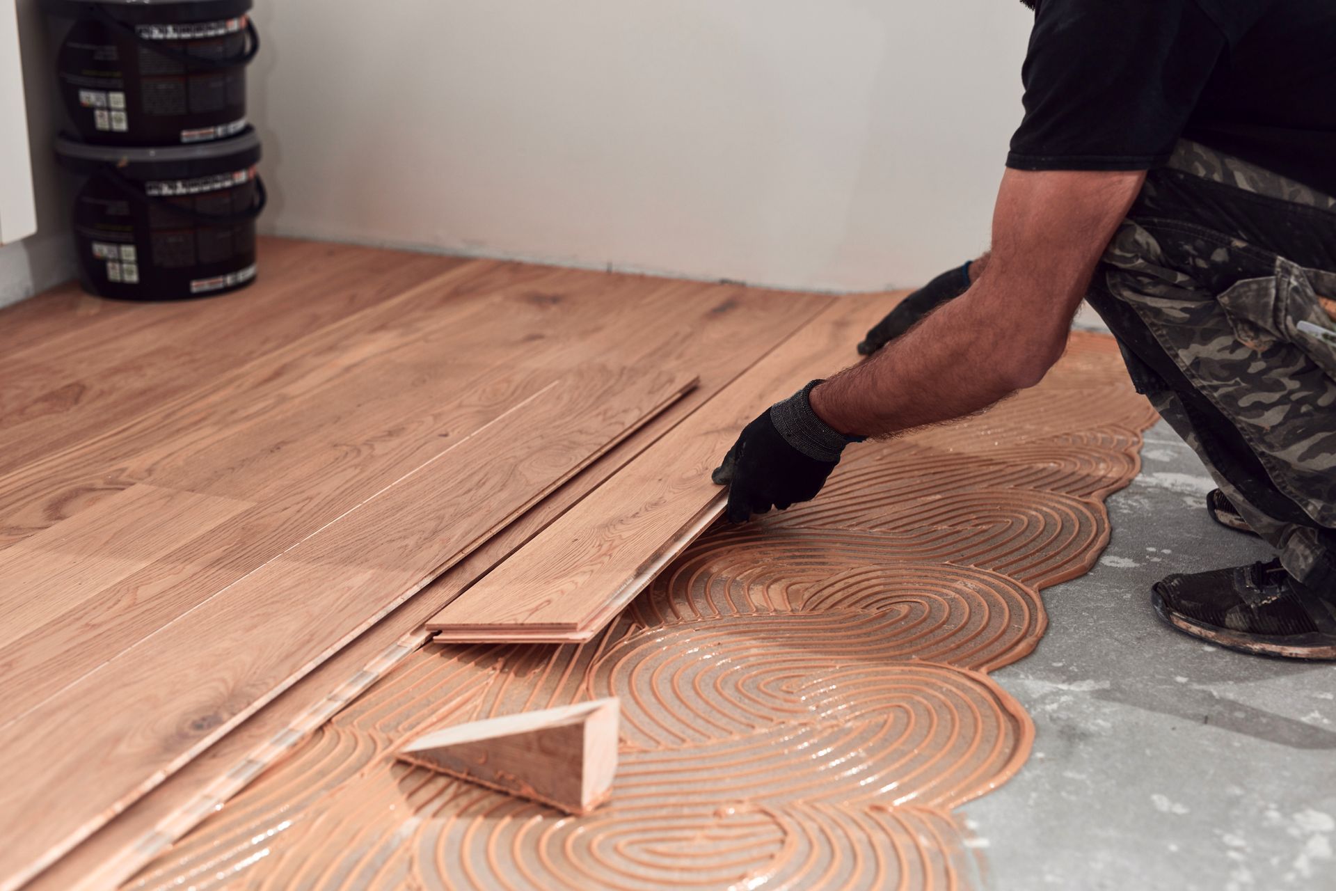 Person installing wood flooring, applying glue in a room.