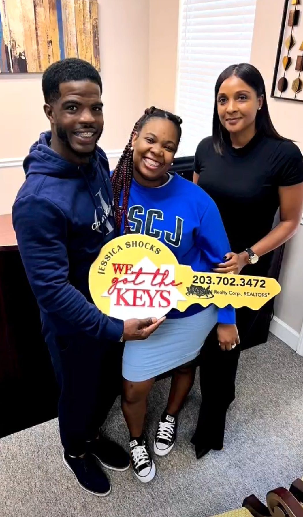 Three people holding a large key-shaped sign. Smiling people in an office.