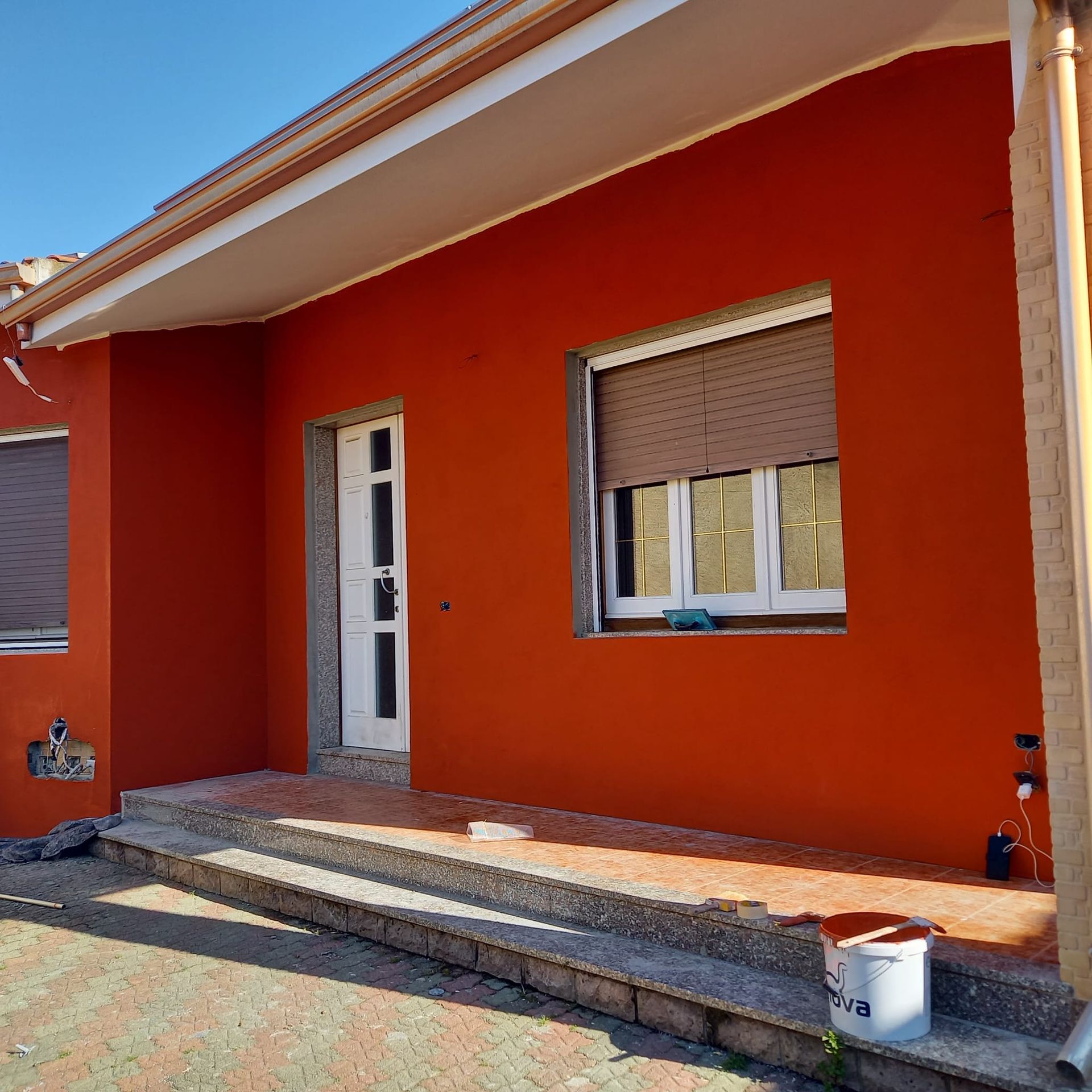 Esterno di una casa arancione con porta bianca, finestre con persiane e un piccolo portico anteriore in costruzione.