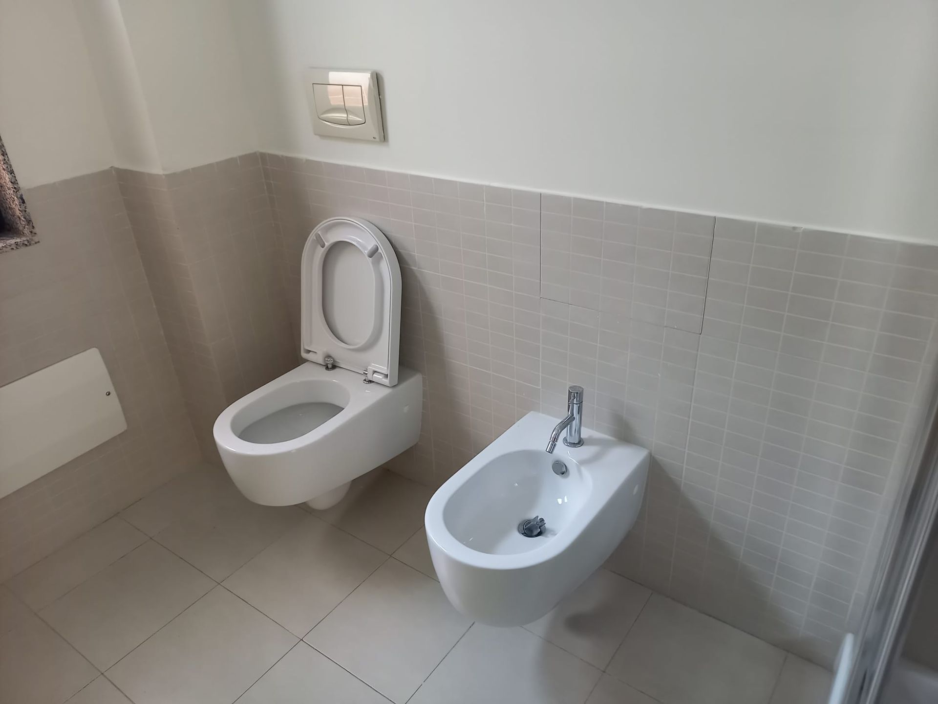 Bagno accessibile con WC e bidet, pareti e pavimento piastrellati di colore chiaro.