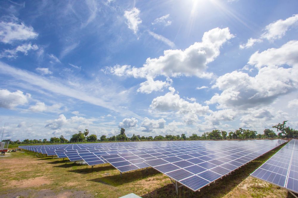 Solar panels in a field under a bright blue sky with scattered clouds