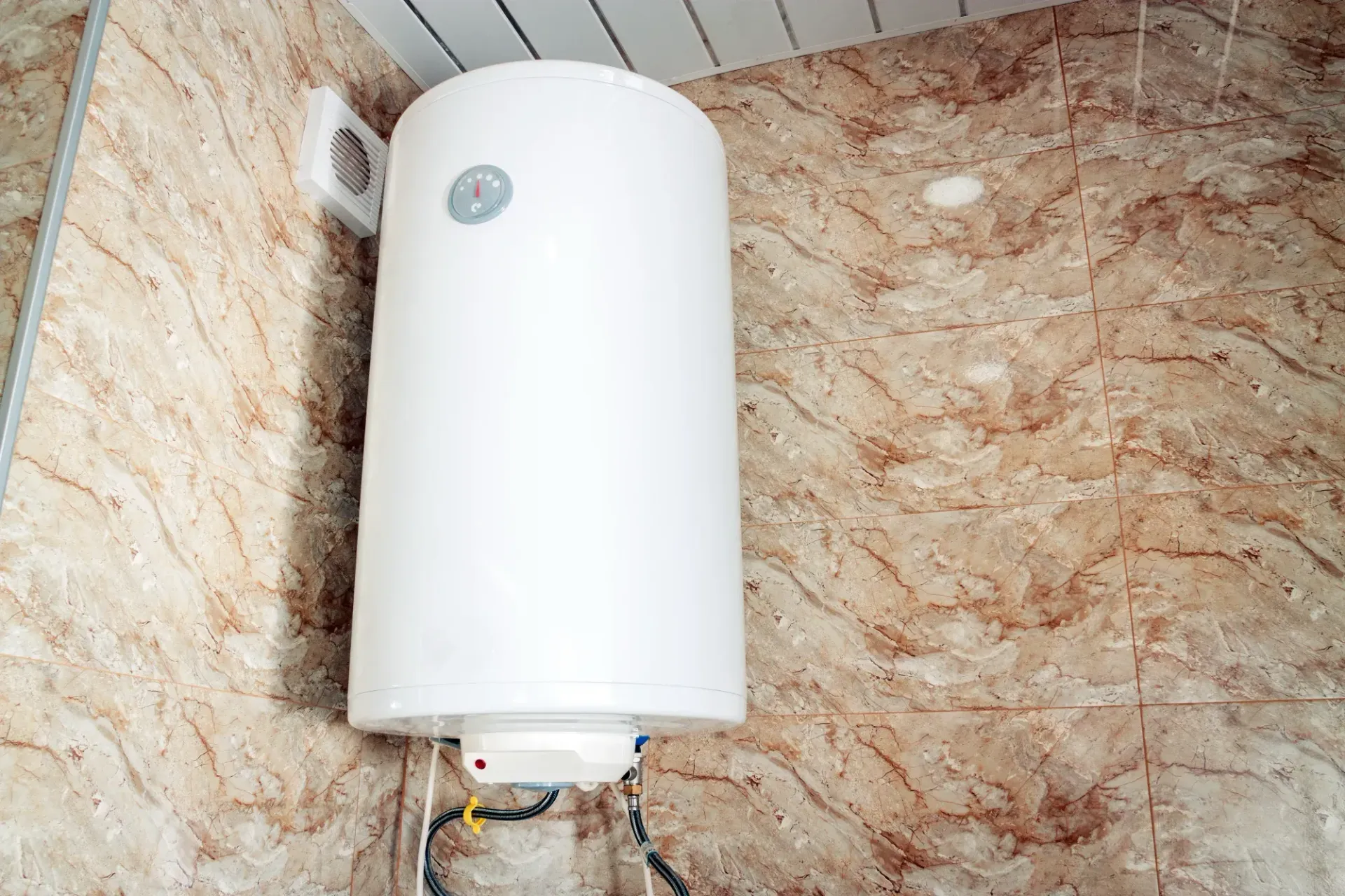 White wall-mounted cylindrical water heater in a tiled bathroom corner — Macleay Energy Solutions In Kempsey, NSW