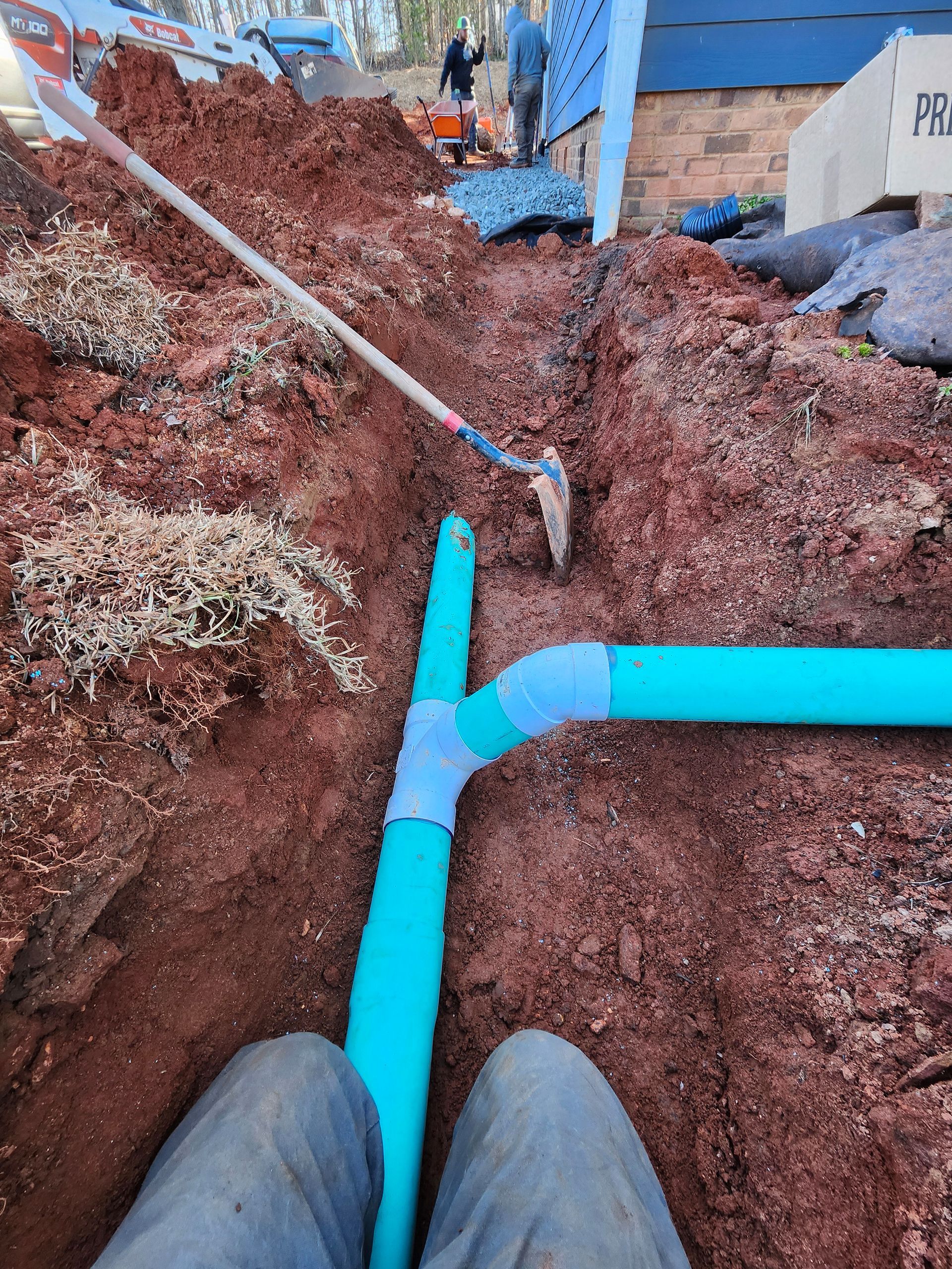 A person is kneeling in the dirt next to a blue pipe.