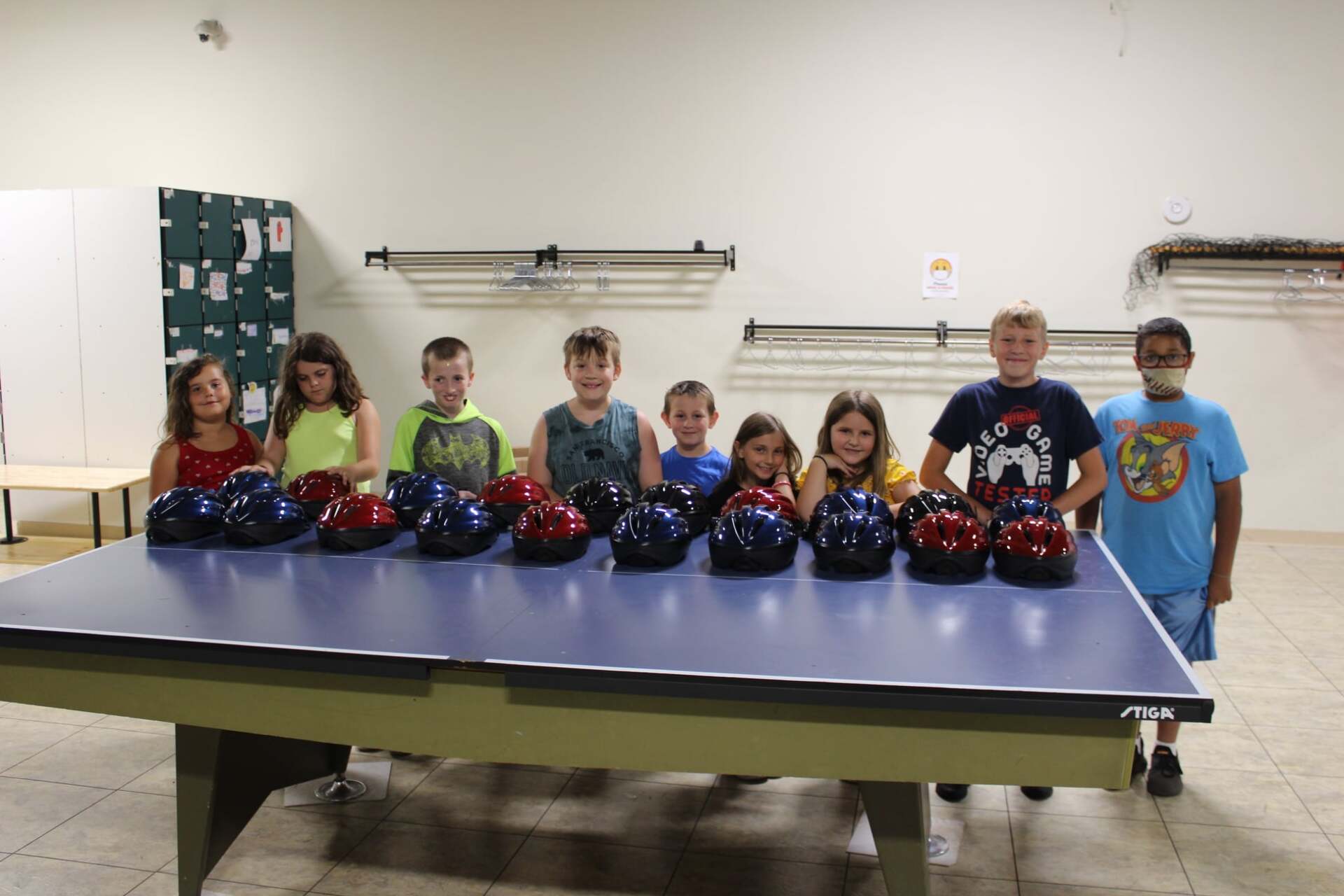 A group of children are standing around a table with bowling balls on it.