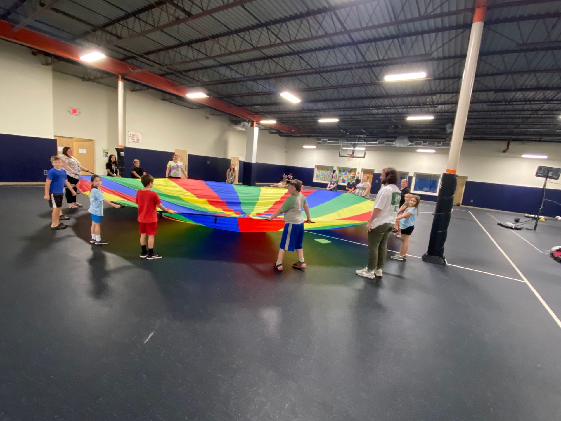 A group of children are playing with a colorful parachute in a gym.