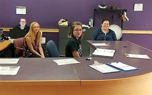 A group of people are sitting at a table in a room with purple walls.