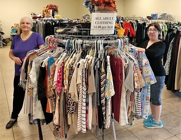 Two women are standing in front of a rack of clothes in a store.