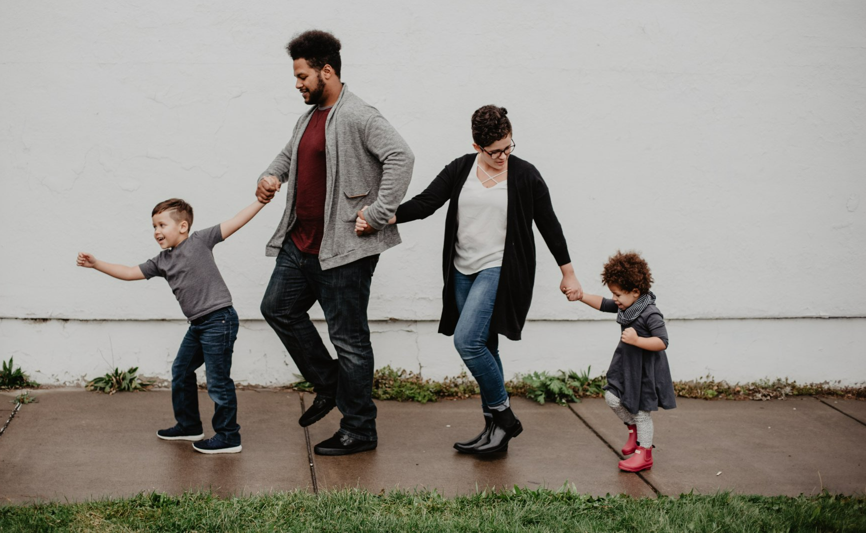 A family is walking down a sidewalk holding hands.