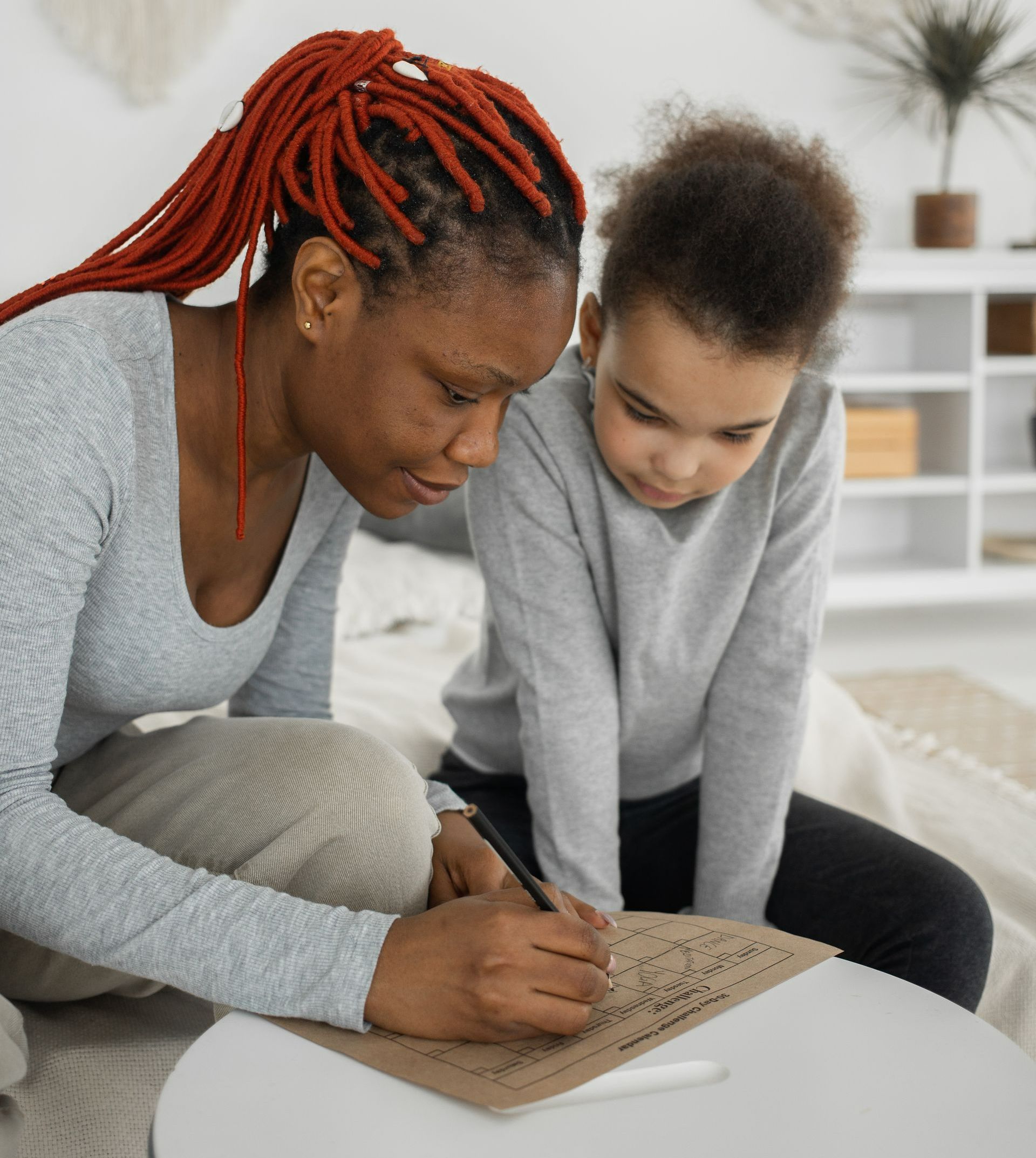 A woman and a child are sitting on the floor writing on a piece of paper.