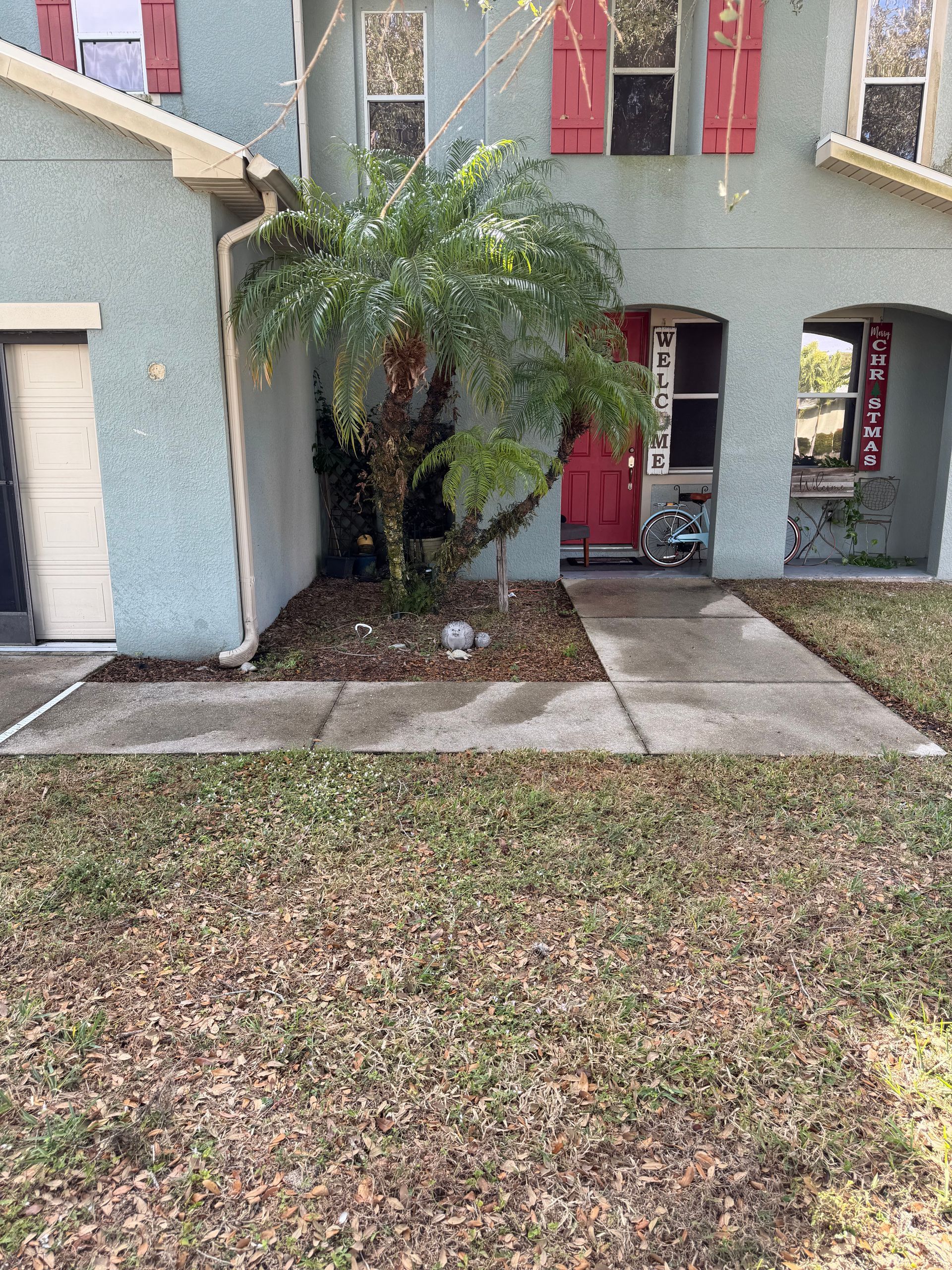 Front view of a pastel townhouse with a red door, arched entryway, and a small palm in the courtyard
