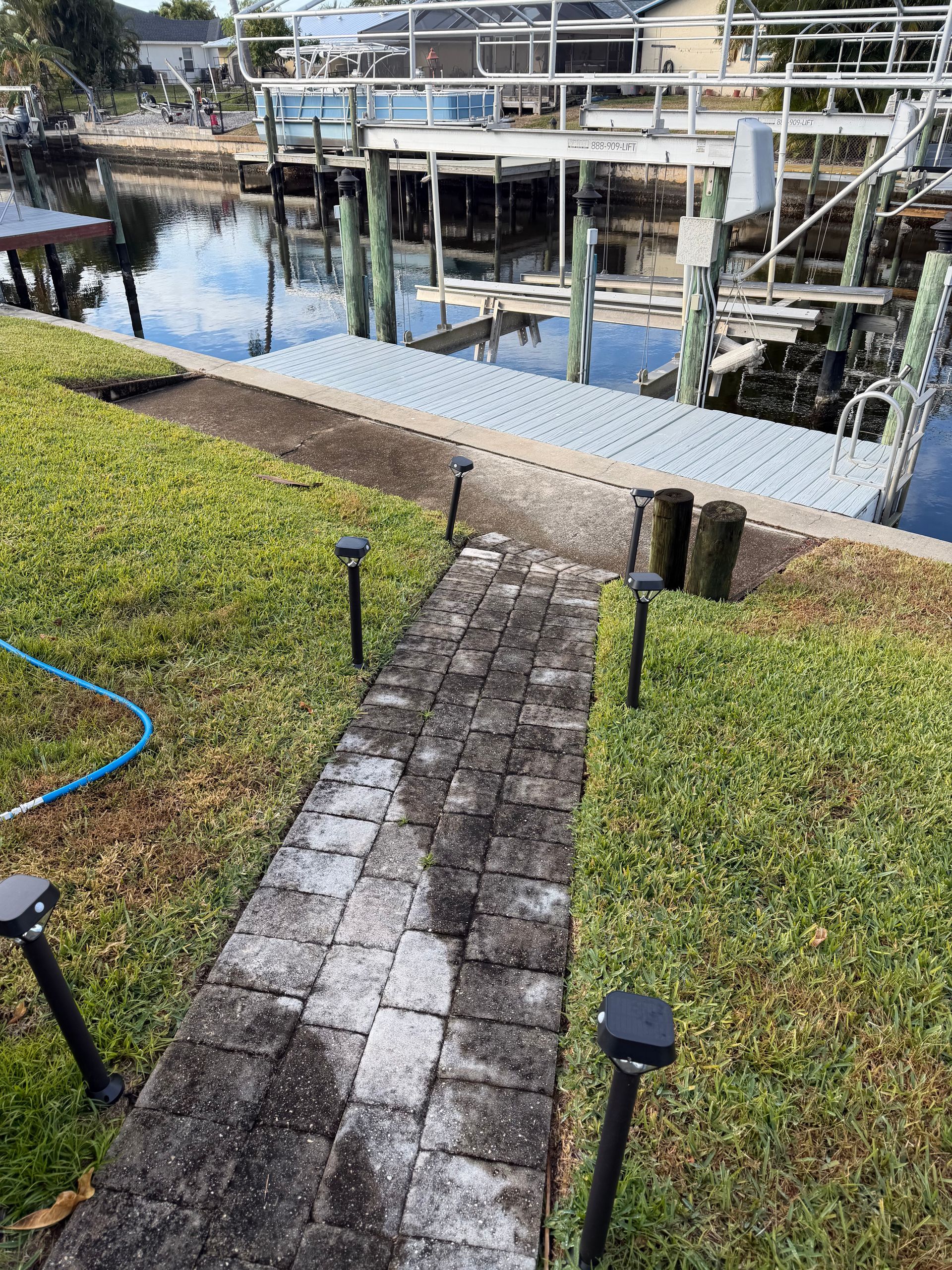 Narrow stone path down a grassy slope to a dock with calm water and boats