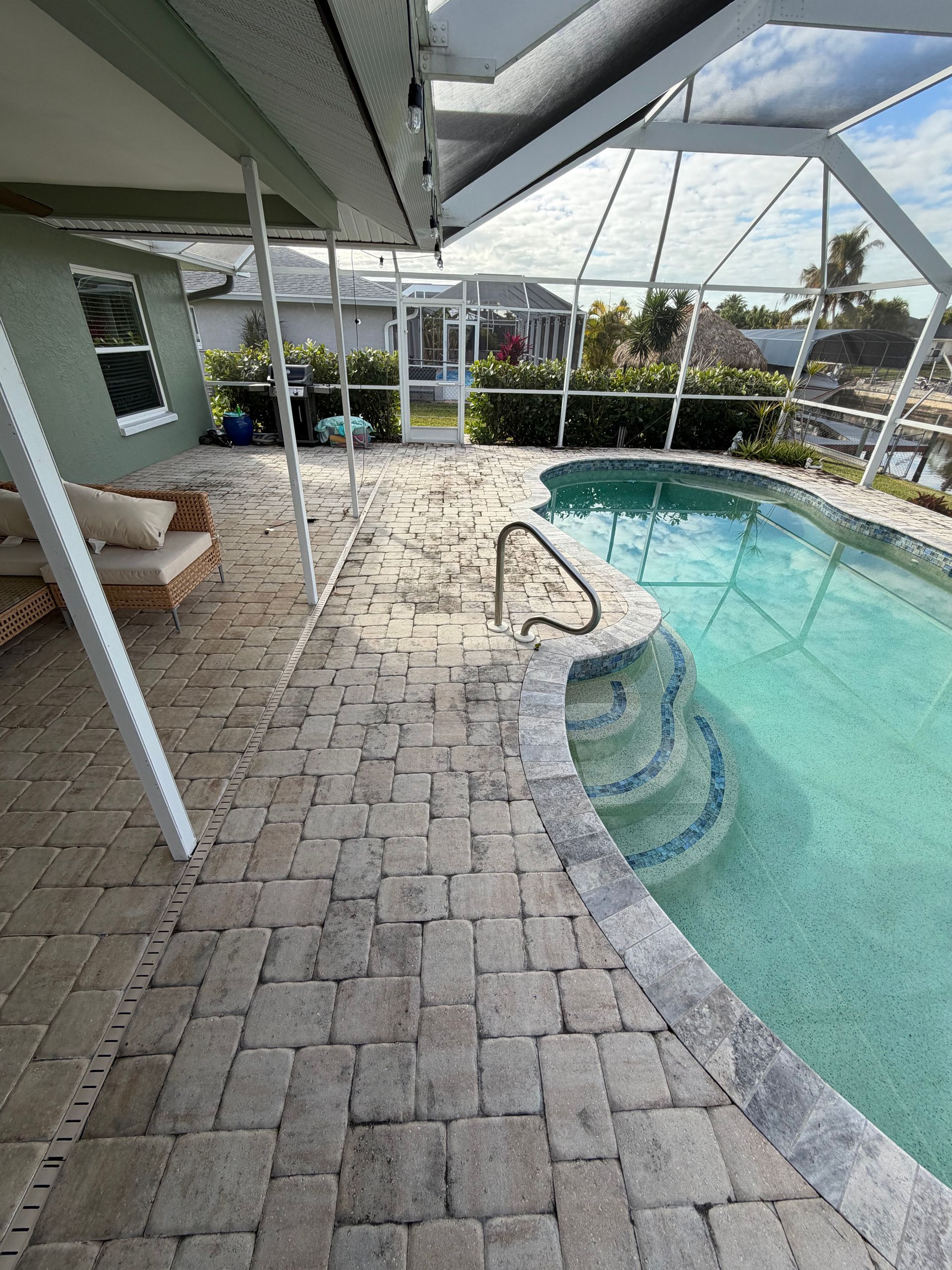 Covered patio with wicker chairs and a screened-in pool with steps and stone pavers