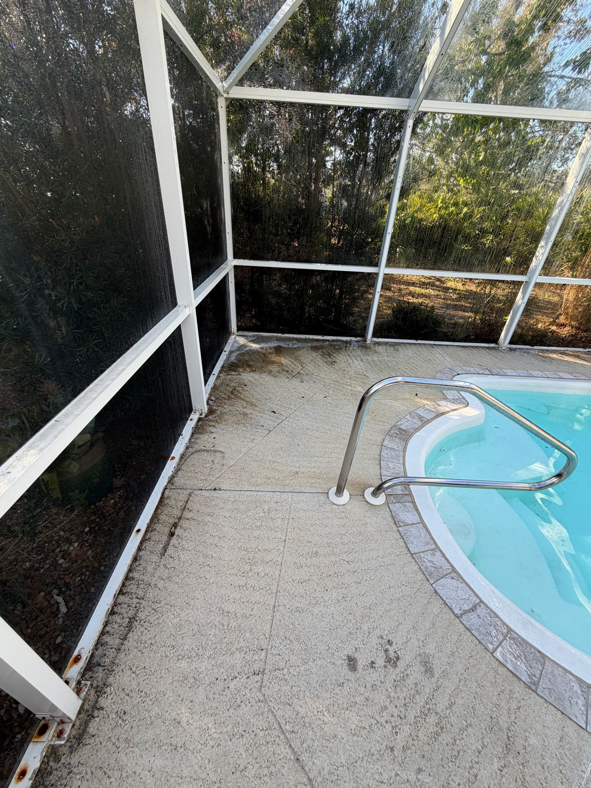 Screened patio beside a swimming pool with a hose on the concrete floor
