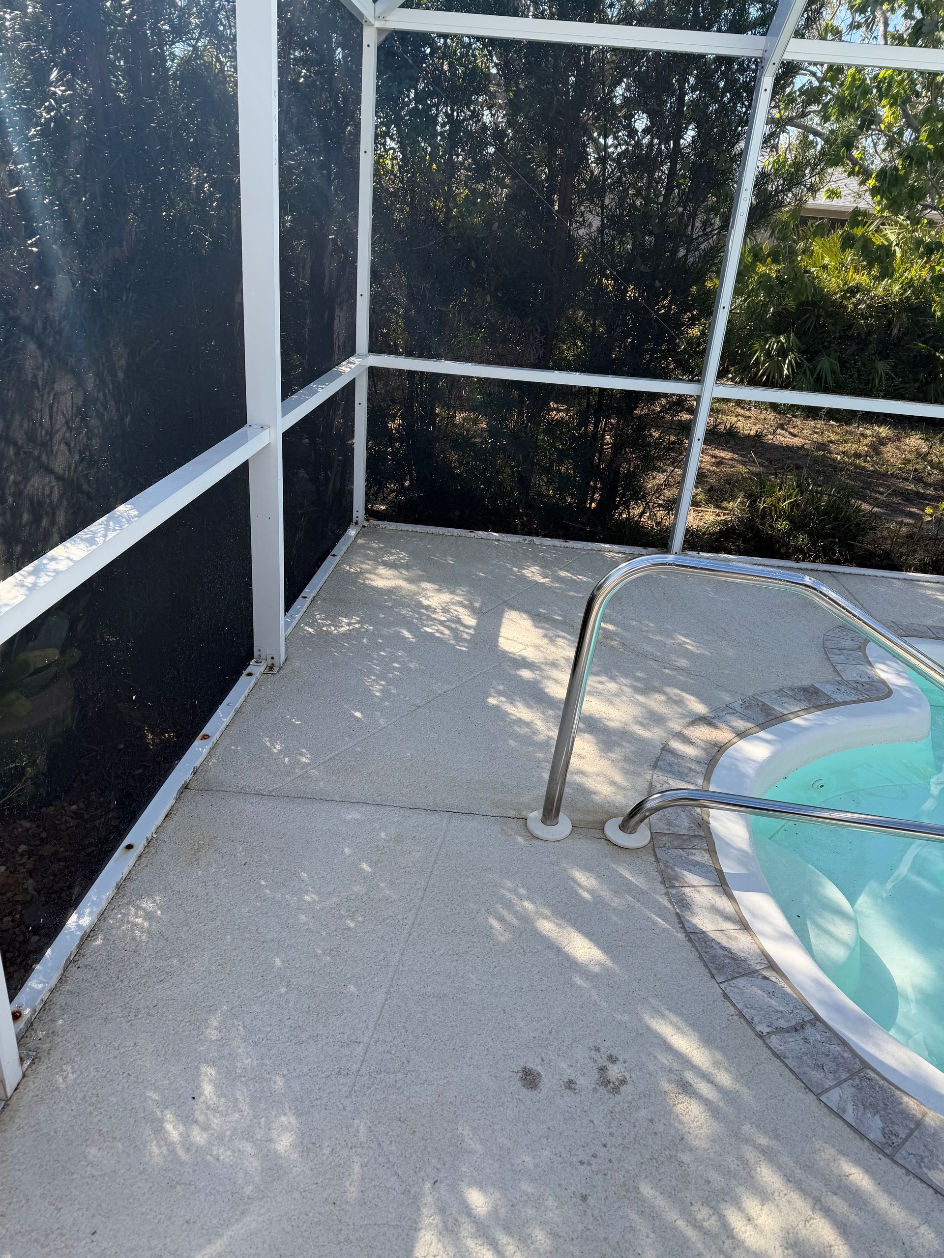 Screened patio with concrete floor, white railing, and a small blue hot tub beside a metal handrail