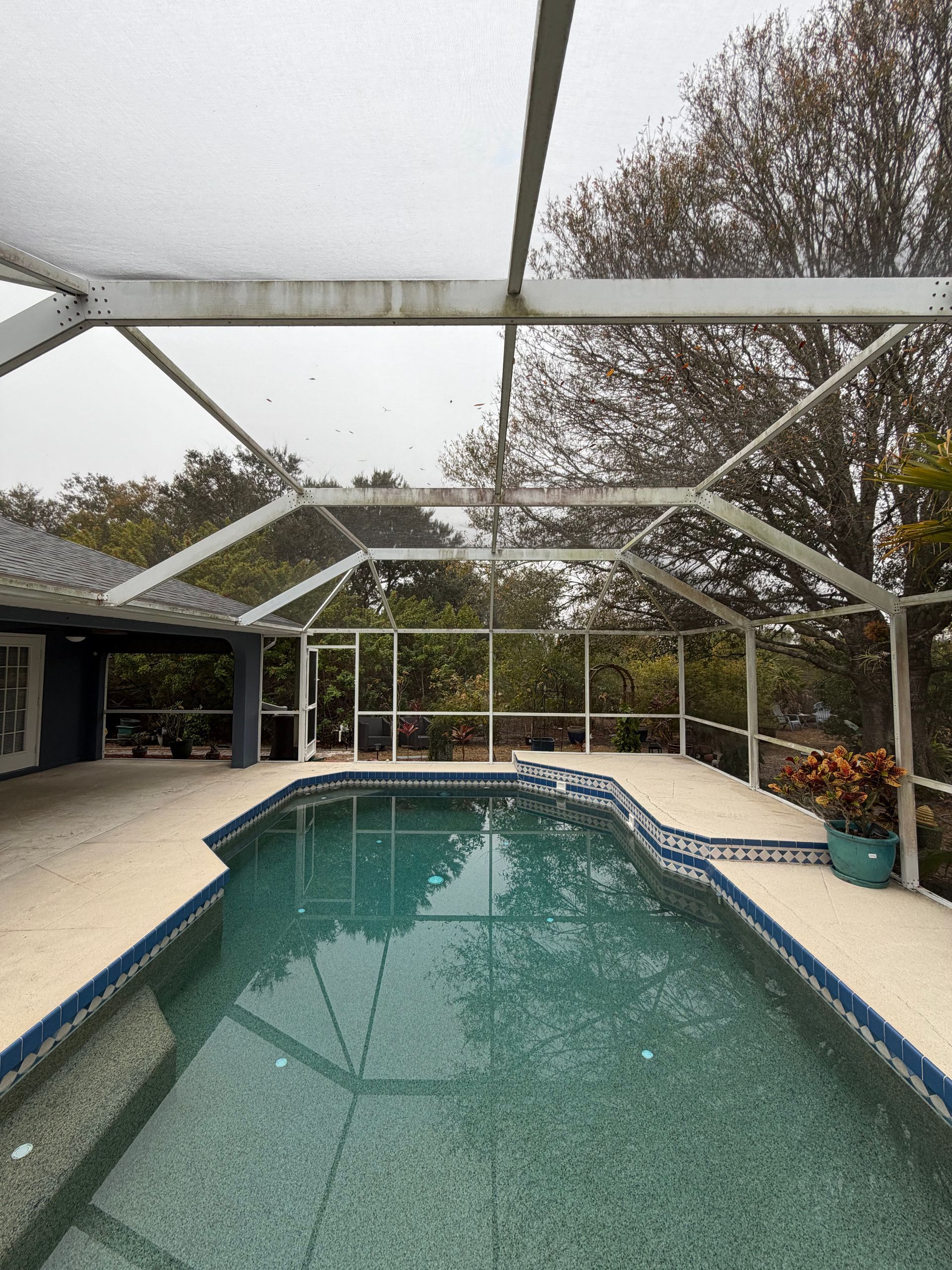 Screened-in backyard pool with turquoise water, white metal frame, and patio lounge area