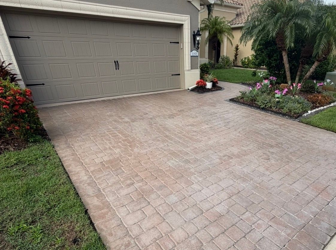 Brick-paved driveway leading to a two-car garage with landscaped garden beds on both sides