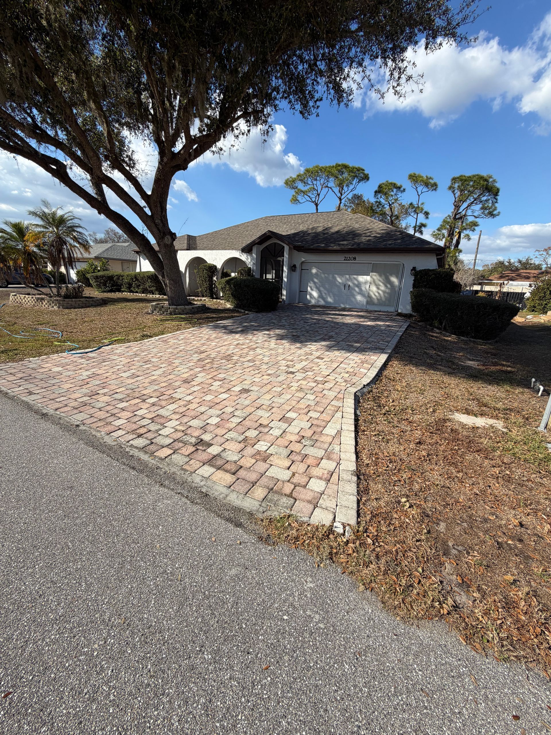 Suburban house with stone driveway, large tree, and blue sky on a sunny day
