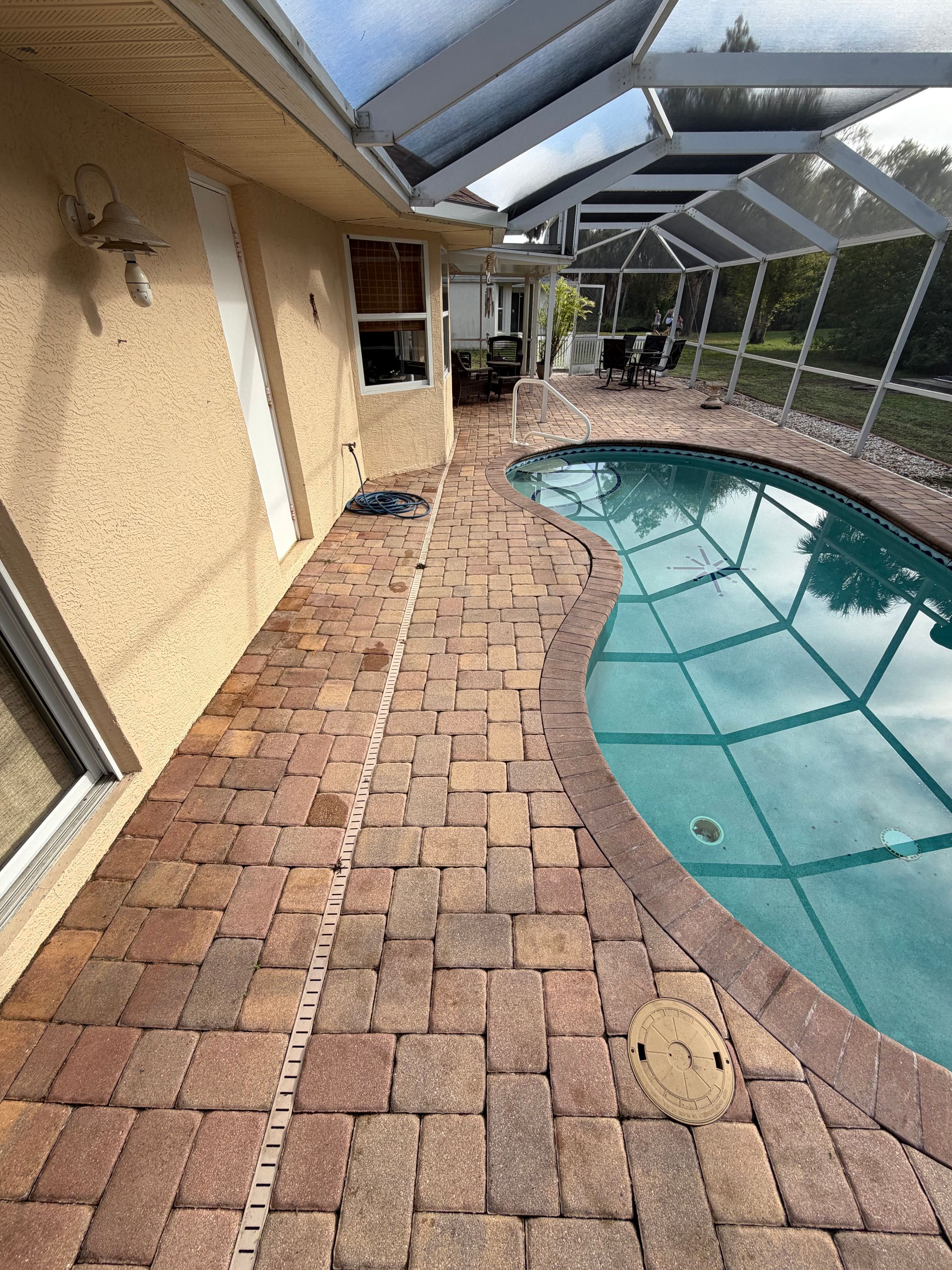Screened backyard patio with a curved in-ground pool and brick paver walkway
