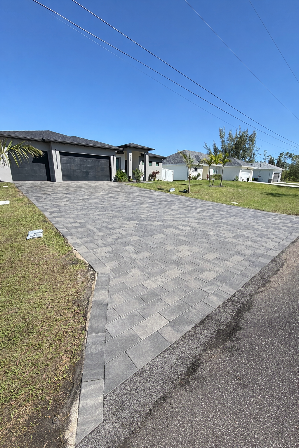 Large gray paver driveway leading to a modern house under a clear blue sky
