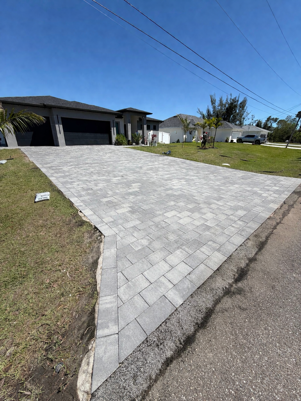 Paved driveway leading to a house, with grass on both sides and a blue sky overhead.