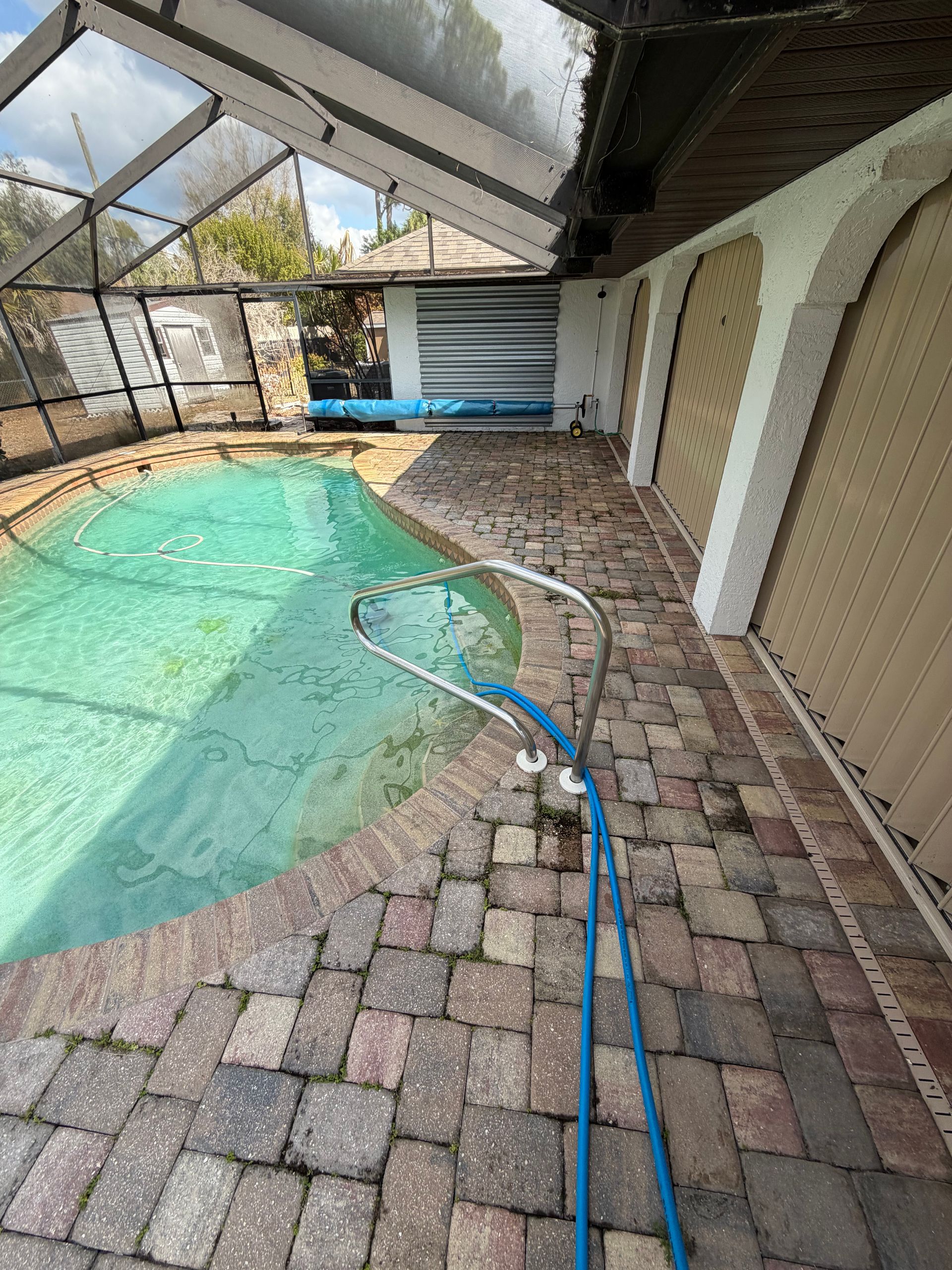 Poolside patio with blue hose and net beside a covered swimming pool