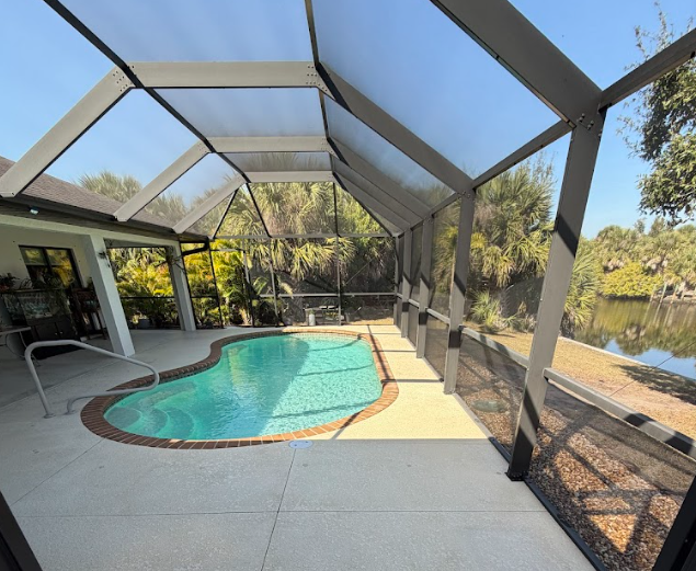 Screened-in backyard pool beside a lake, with a covered patio and stone deck.