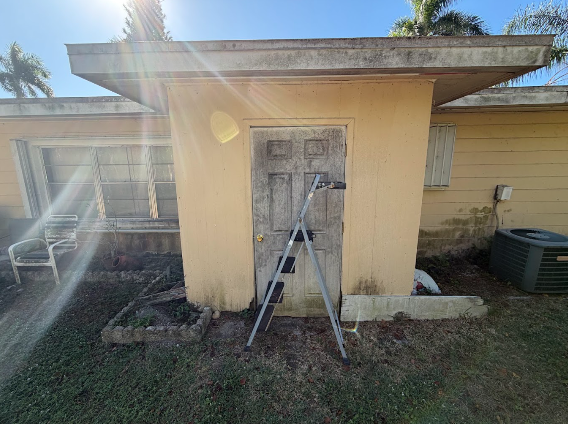 Ladder leaning against a yellow house’s front door in bright sunlight