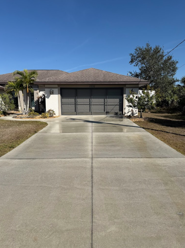 Suburban house with two-car garage and long concrete driveway under a clear blue sky