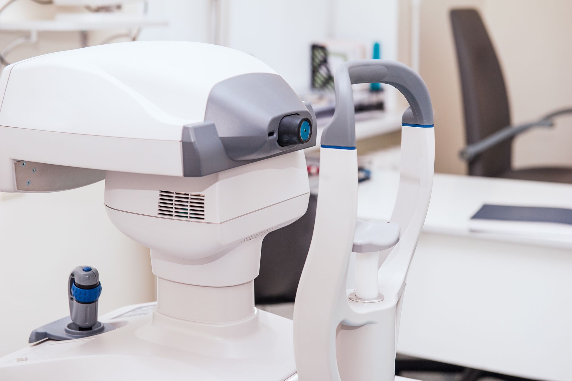 Dispositivo robotico da laboratorio di colore bianco su una scrivania in un ambulatorio, con un sensore blu e una sedia sullo sfondo.