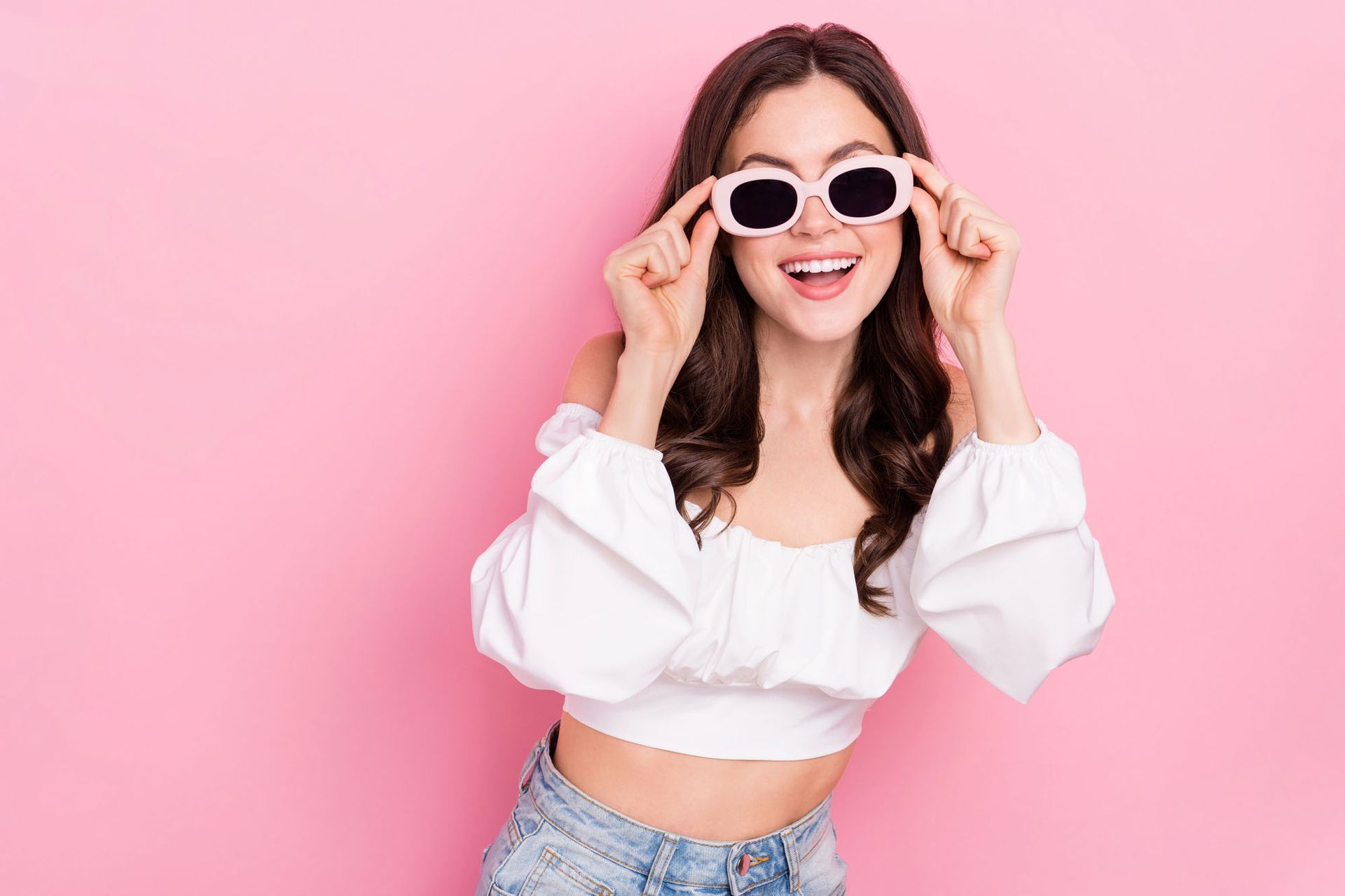 Donna con occhiali da sole bianchi e top corto sorridente su sfondo rosa