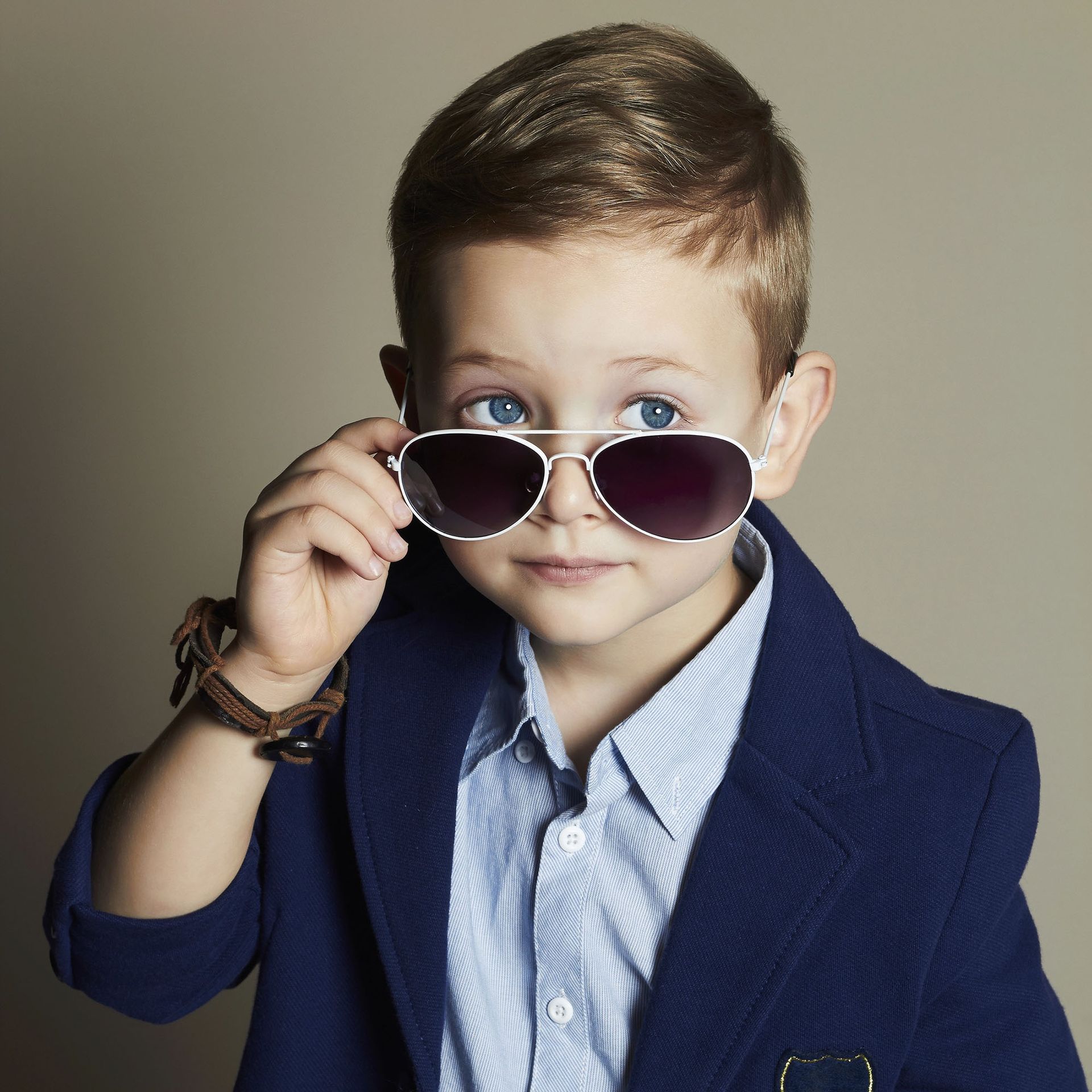 Bambino con blazer blu e occhiali da sole, che guarda in camera con espressione neutra.