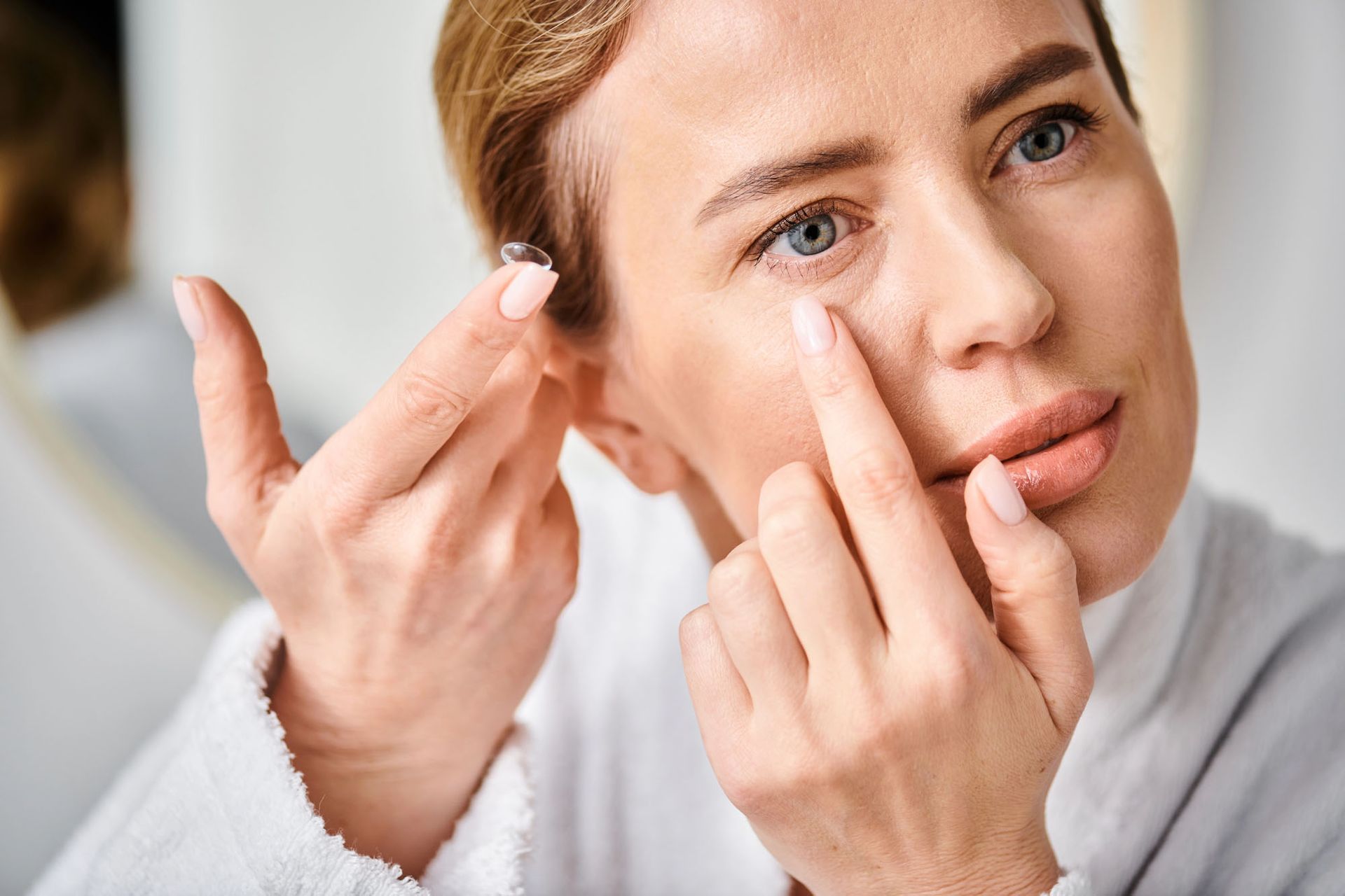 Donna che si applica una lente a contatto davanti allo specchio del bagno.