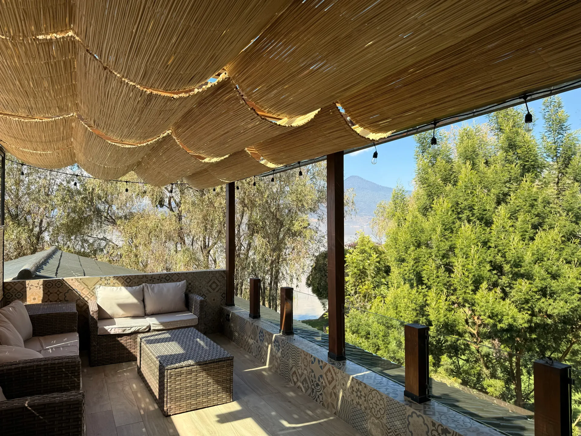 Un patio con sofá, mesa y sillas bajo un dosel con árboles al fondo.