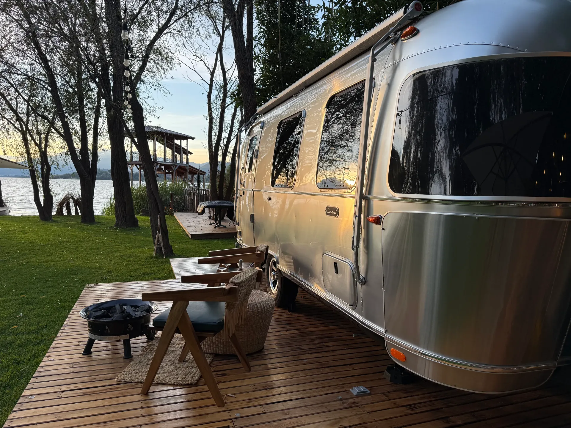 Un remolque Airstream plateado está estacionado en una plataforma de madera al lado de un lago.