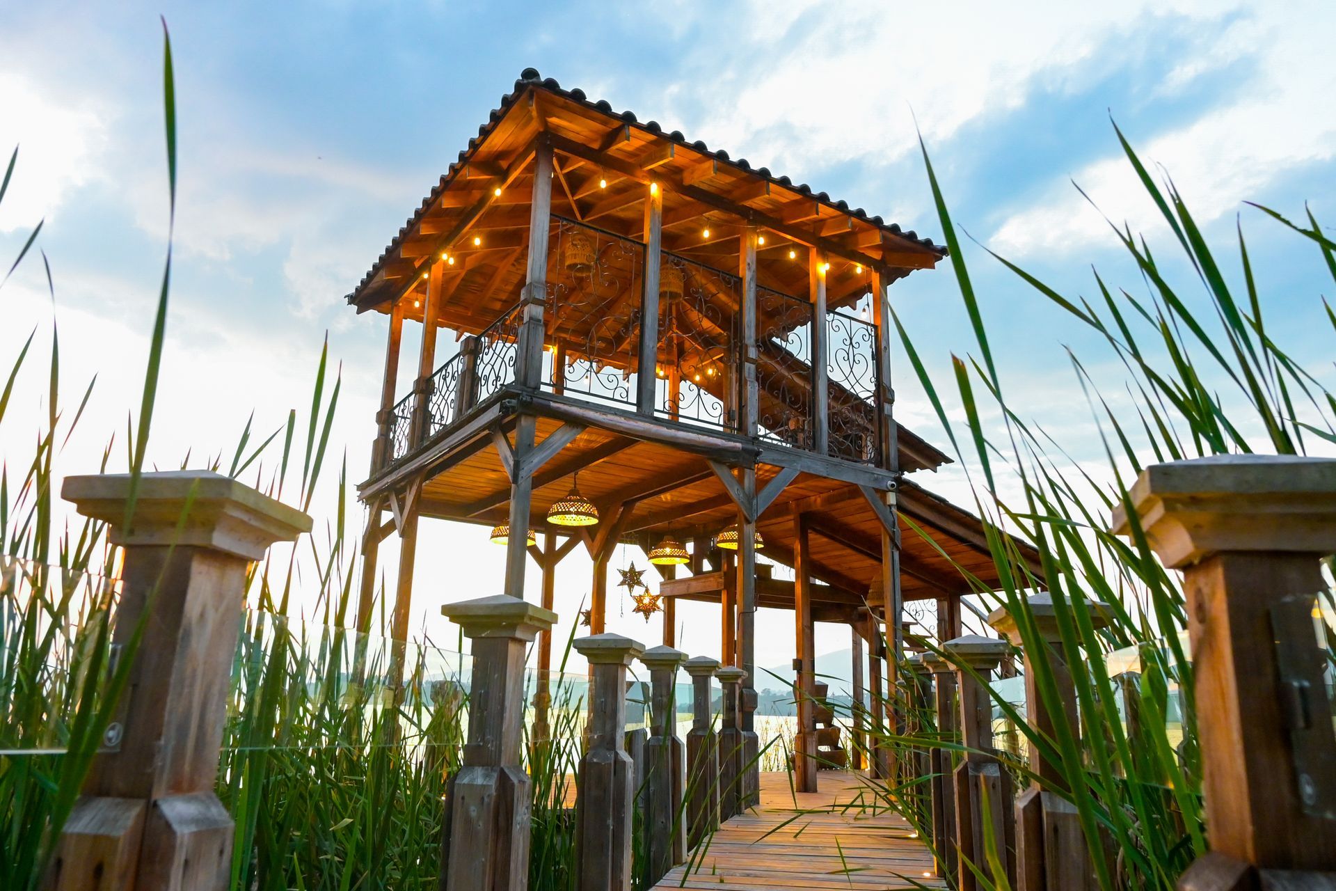 A wooden structure with lights on the roof is surrounded by tall grass.