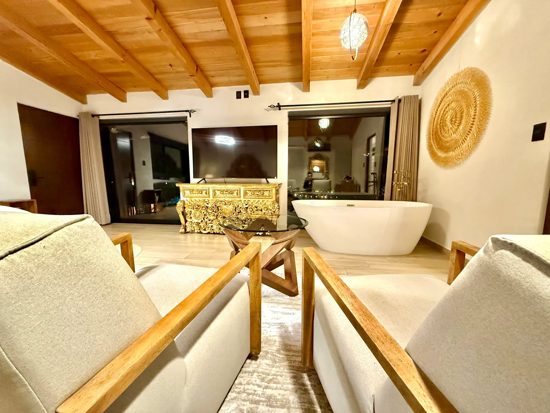 Una sala de estar con bañera, sillas, televisión y techo de madera.