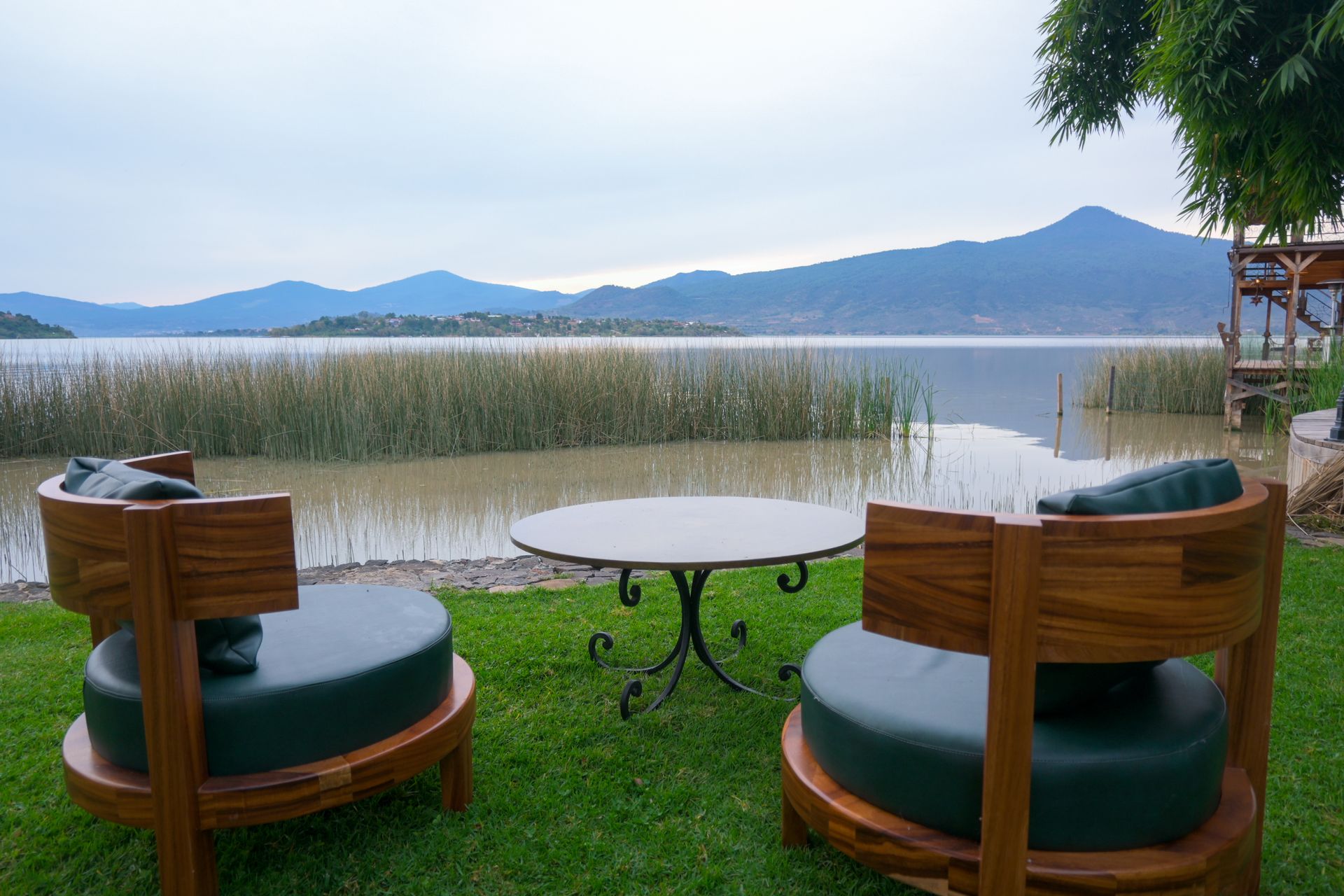 Dos sillas y una mesa están sentadas en un exuberante césped verde junto a un lago.