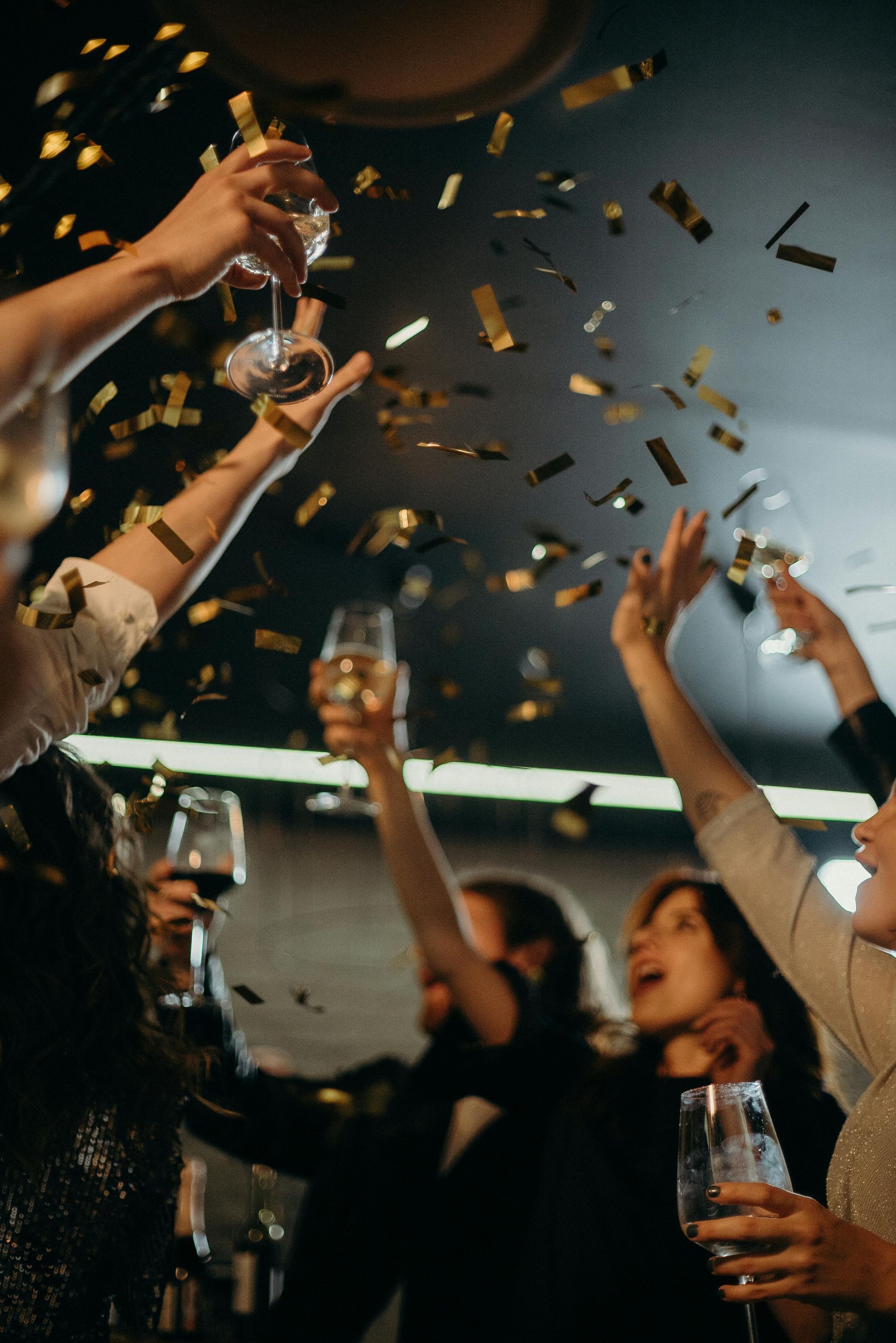 Un grupo de personas sostiene copas de vino y lanza confeti al aire.