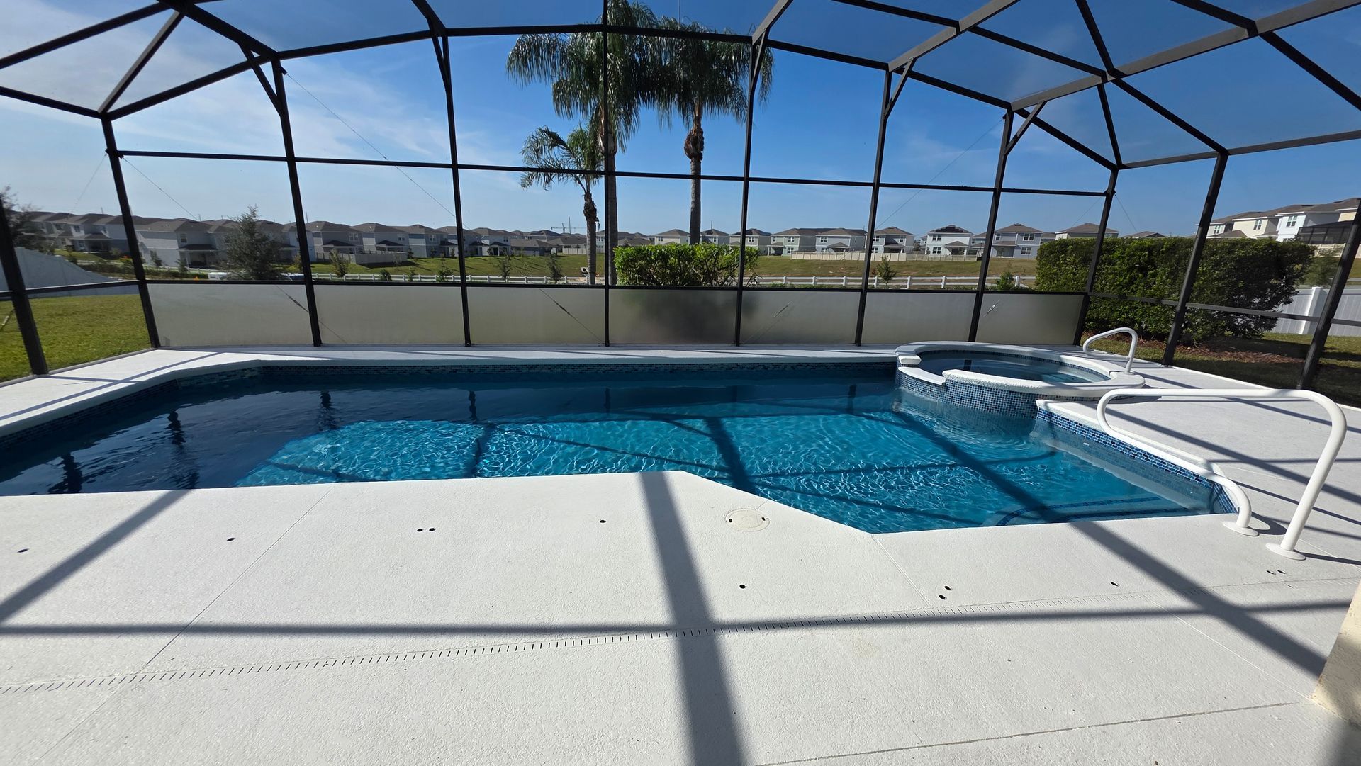 Swimming pool with jacuzzi inside a screened enclosure; sunny outdoor setting.