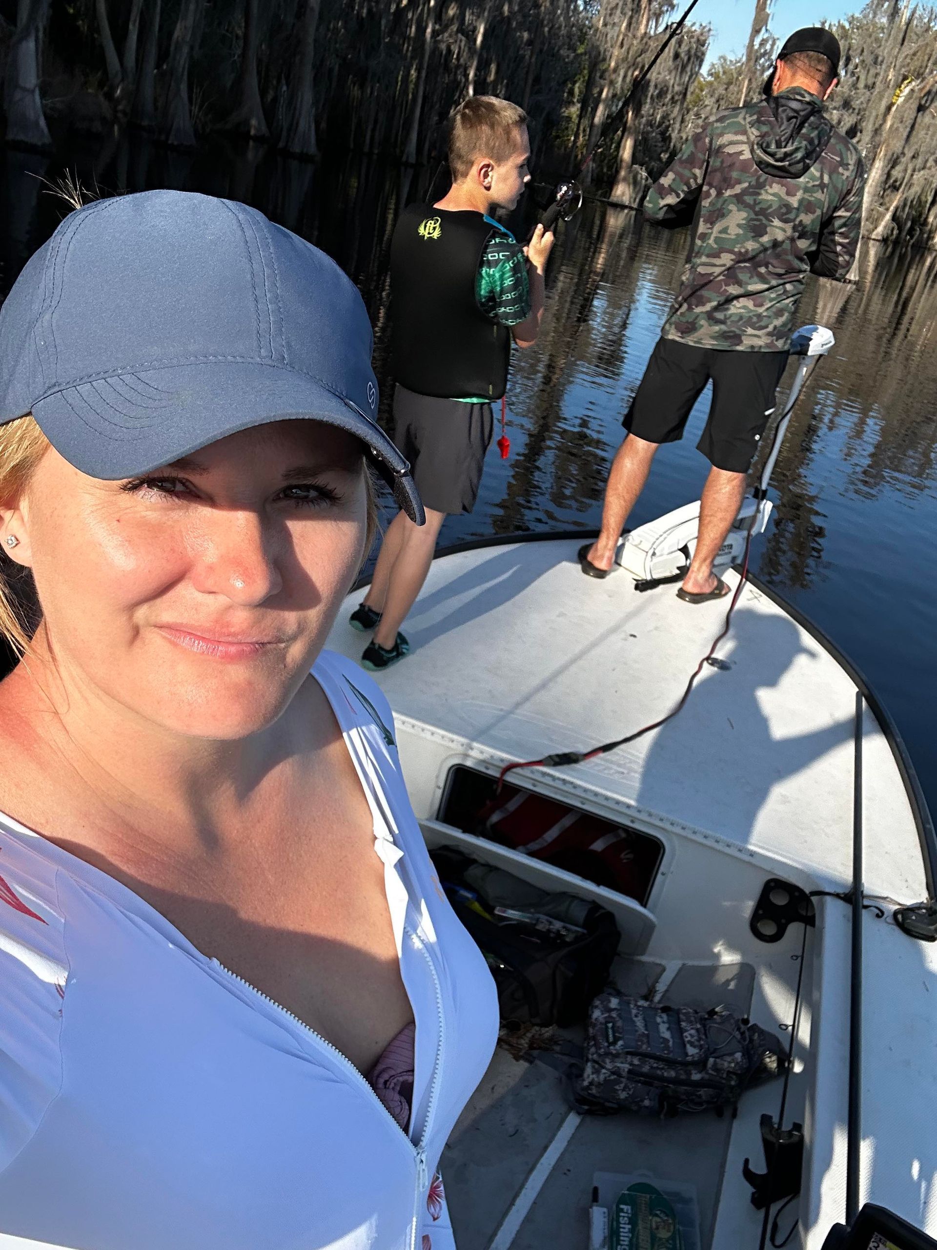 A woman is standing on the back of a boat with two men fishing in the background.