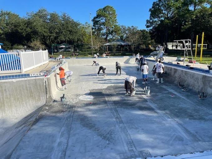 Construction workers repairing a drained swimming pool.  They are applying materials to the concrete surface on a sunny day.