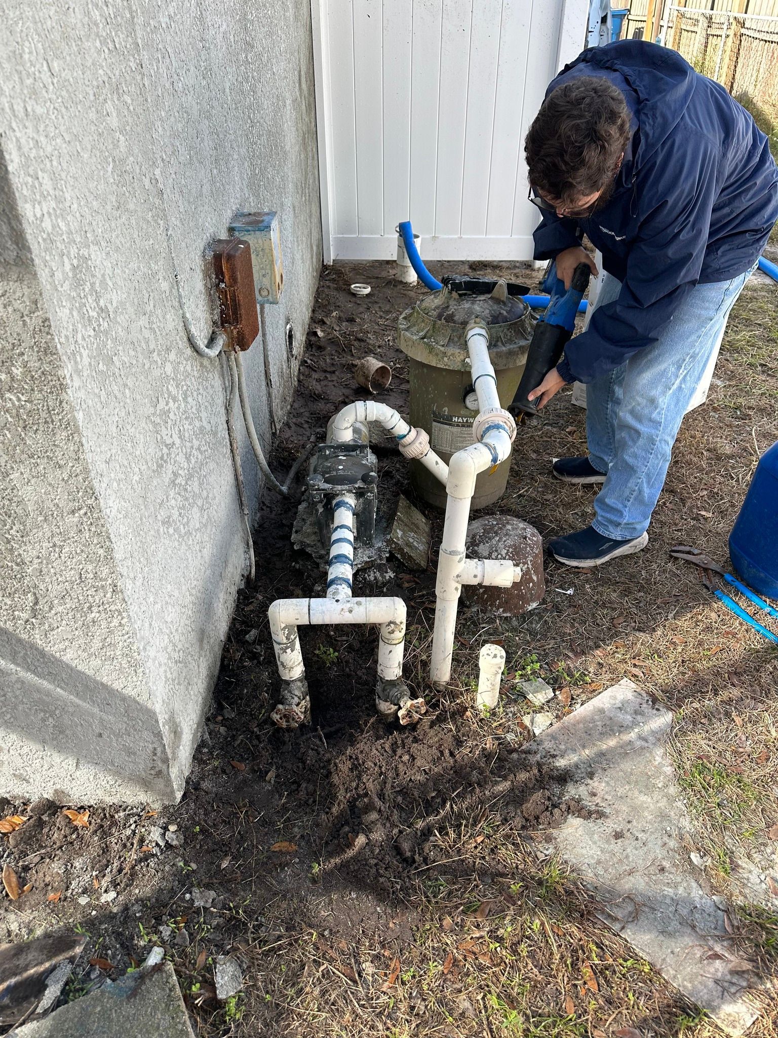 Person working on pool equipment near a fence and wall.