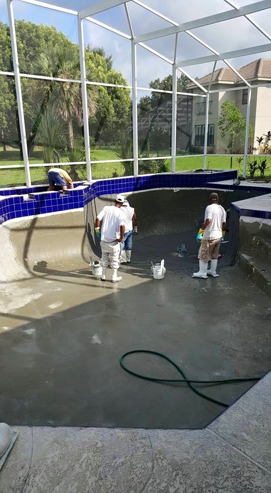 Workers resurfacing a concrete swimming pool, applying materials. Blue tile trim, white screen enclosure.