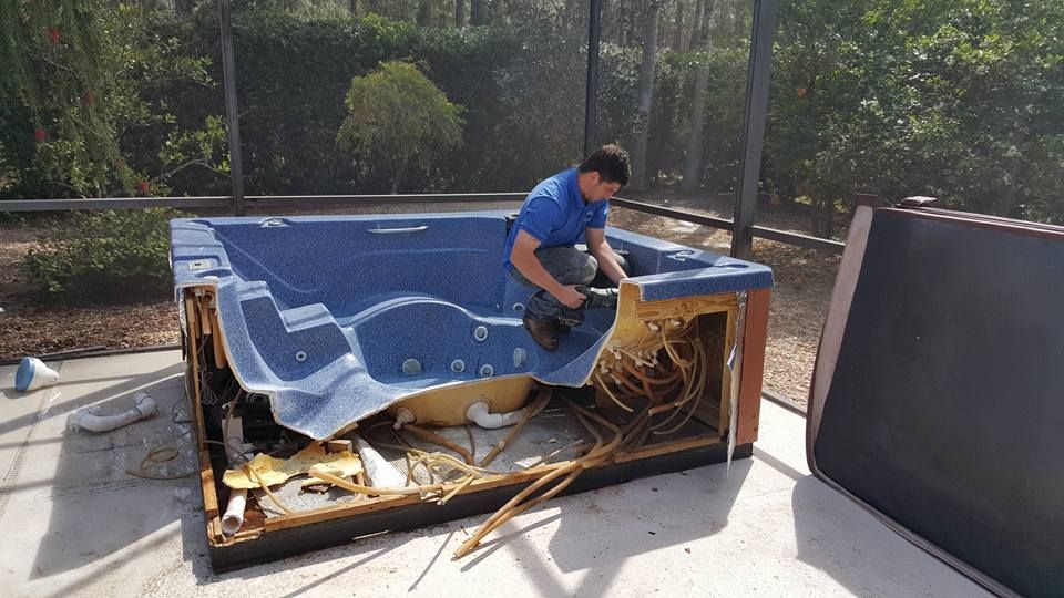 Man repairing a partially dismantled hot tub outdoors.