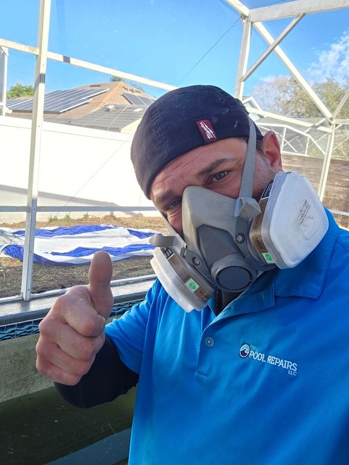 Man in blue shirt and respirator giving a thumbs-up on a boat dock, with a roof structure in the background