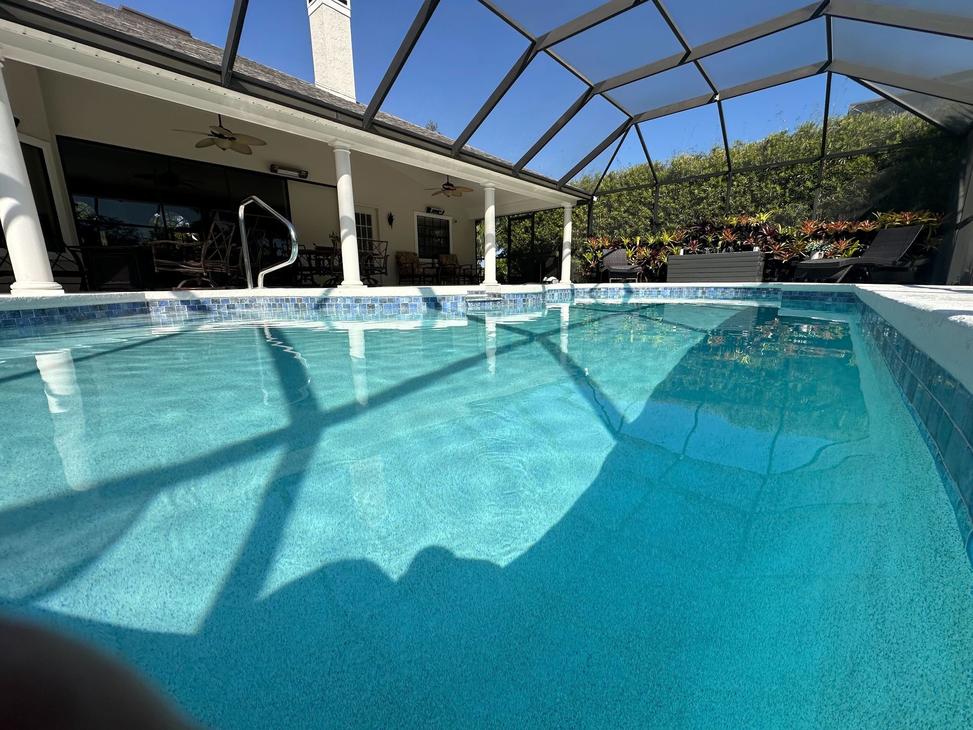 Swimming pool under a screened enclosure with a house in the background and a blue sky.