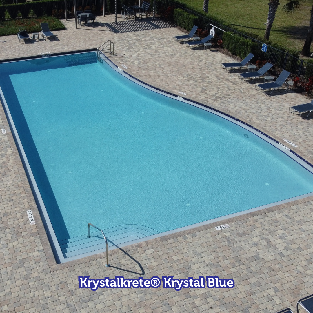 Swimming pool with blue water surrounded by beige paving stones and lounge chairs.